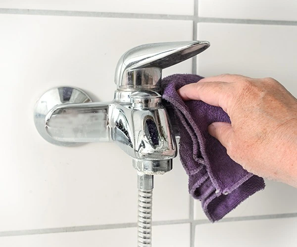 Foto de alguien limpiando la cal del grifo de un baño